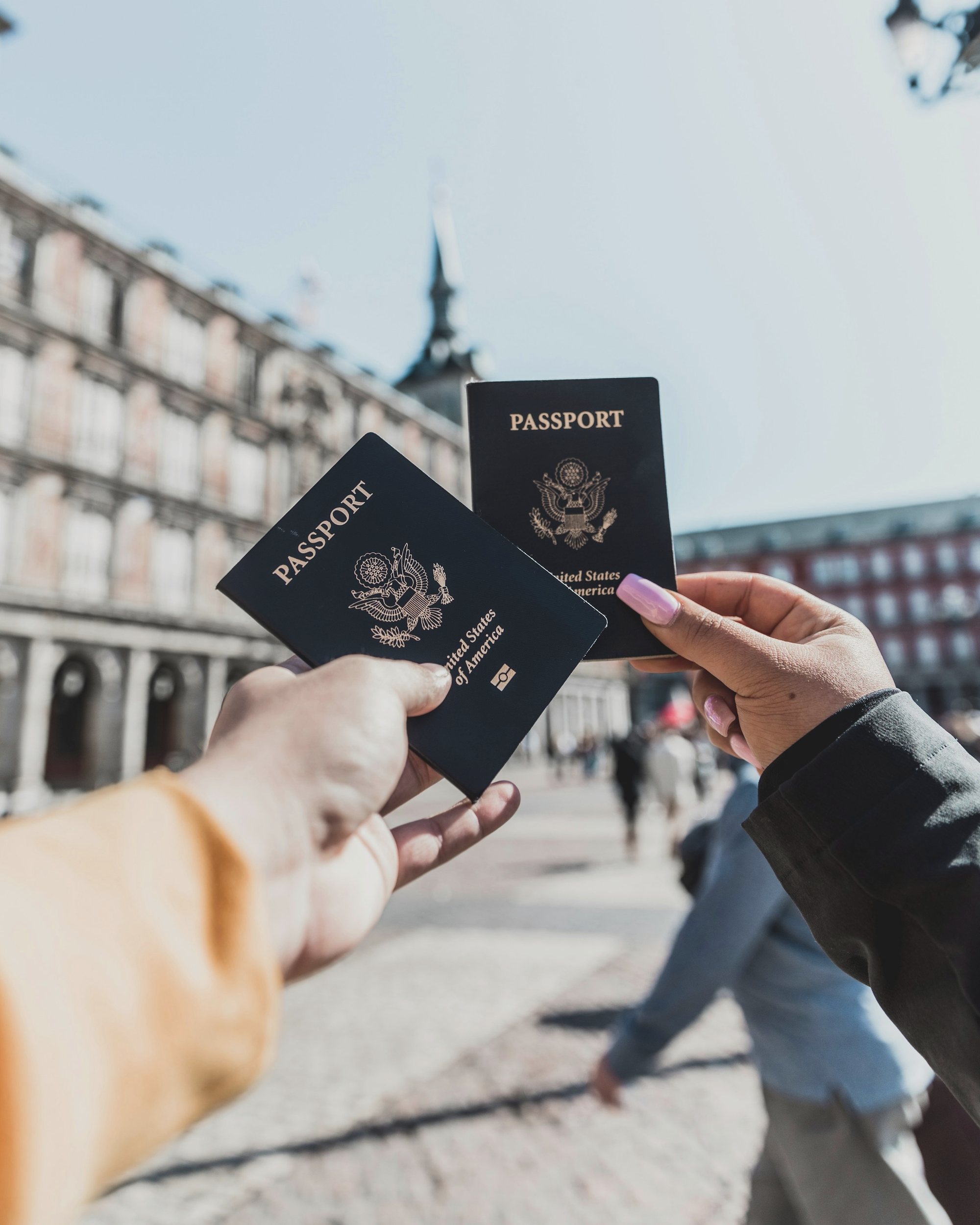 Dos pasaportes sostenidos frente a una plaza urbana